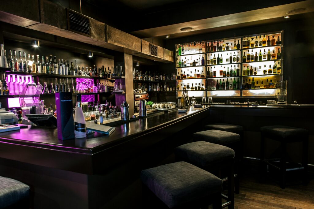 Cozy bar setting with illuminated shelves and a variety of bottles for a stylish ambiance.